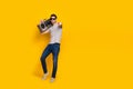 Full size photo of nice brunet millennial guy hold boombox wear t-shirt jeans sneakers isolated on yellow background