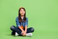 Full size photo of nice little girl sit look promo wear shirt jeans hairband footwear isolated on green background Royalty Free Stock Photo