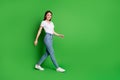 Full size photo of nice successful brunette hair young woman walking around wear t-shirt jeans shoes isolated on green