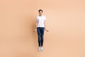 Full size photo of optimistic brunet man jump wear t-shirt jeans sneakers isolated on beige background Royalty Free Stock Photo