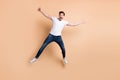 Full size photo of optimistic brunet man jump yell wear t-shirt jeans sneakers isolated on beige color background Royalty Free Stock Photo