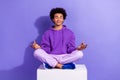 Full size photo of peaceful relaxed person wear stylish pullover sit on cube in meditation pose isolated on purple color