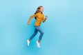 Full size photo of positive girl blond hair wear yellow pullover denim pants running look empty space  on blue Royalty Free Stock Photo