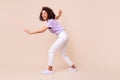 Full size photo of positive lovely girl dressed striped t-shirt white trousers sneakers sneaky walk isolated on beige