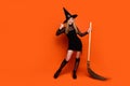 Full size photo of pretty blonde teenager girl hold broom thumb up dressed black halloween outfit isolated on orange Royalty Free Stock Photo