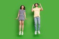 Full size photo of young couple happy positive smile have fun jump rejoice success isolated over green color background