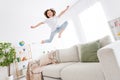 Full size photo of young excited small girl happy positive smile have fun jump up fly air sofa indoors