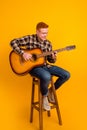 Full size photo of young handsome man sit stool play guitar performance stage isolated over yellow color background