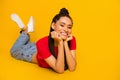 Full size portrait of charming dark skin girl lying floor arms on cheeks look camera isolated on yellow color background Royalty Free Stock Photo