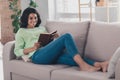 Full size profile photo of charming dark skin girl lying on couch hold book toothy smile weekend home indoors