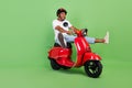 Full size profile side photo of young african man ride scooter crazy speed isolated over green color background