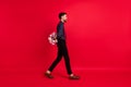 Full size profile side photo of young happy gentleman go walk hide bouquet behind back isolated on red color background
