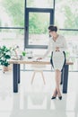 Full size of successful feminine brown haired economist professional in formal wear, sitting on top of her desk at work station i Royalty Free Stock Photo