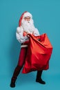 Full size of Surprised stylish Santa Claus holds huge red bag with many presents on Christmas. New Year concept Royalty Free Stock Photo