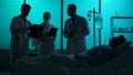 Full-sized silhouette shot of three doctors standing around a patient on a breathing support, in coma, laying in a