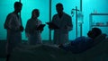 Full-sized silhouette shot of three doctors standing around a patient laying in a hospital bed in front of them. Doctors