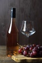 A full, unopened bottle of rose wine next to an empty glass goblet and a bunch of red grapes. Vertical orientation Royalty Free Stock Photo