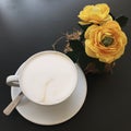 A cup of capuccino coffee on a table with yellow flowers