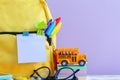 Full yellow school backpack with stationery on table on purple background