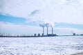 Fuming chimneys of factory on background of blue sky with clouds, and white snow