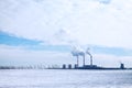 Fuming chimneys of factory on background of blue sky with clouds, and white snow