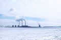 Fuming chimneys of factory on background of blue sky with clouds, and white snow