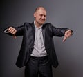 Fun comic bald business man in black suit showing the finger success thumb down sign on grey background. Closeup Royalty Free Stock Photo