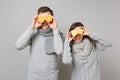 Fun couple girl guy in gray sweaters, scarves together hold orange lemon isolated on grey wall background studio