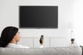 Fun in the evening. Relaxed black lady watching TV pointing remote control at flatscreen television with black screen