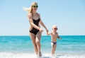 Beautiful young mother and small son holding hands running on the waves on the beach.Fun,family,friendly summer vacation. Royalty Free Stock Photo