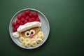 Winter food for kids. Christmas Santa pancake with raspberry and banana for children menu, green background, copy space