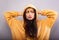 Fun grimacing confused woman posing in fashion yellow hoodie looking unhappy in hood on the head on purple bright background with Royalty Free Stock Photo