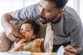 Handsome single young father feeding spaghetti for his mixed race daughter while baby girl sitting on high chair. Infant cute