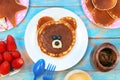 Fun idea for kids breakfast. Bear shaped pancakes with berries and chocolate paste on blue wooden table, top view Royalty Free Stock Photo