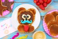 Fun idea for kids breakfast. Bear shaped pancakes with berries and chocolate paste on blue wooden table, top view Royalty Free Stock Photo