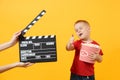 Fun kid baby boy showing thumbs up holding bucket of popcorn, eating fast food isolated on yellow background. Childhood