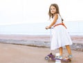 Fun little girl in dress on the scooter in the city