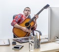 Fun male independent enjoying playing guitar at his computer desk