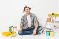 Fun man in newspaper hat with pencil behind ear sitting on floor with instruments for renovation apartment isolated on Royalty Free Stock Photo