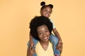 Portrait of happy African baby girl sitting on her mom& x27;s shoulders and having fun, laughing to camera on isolated yellow Royalty Free Stock Photo