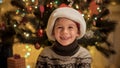 Fun smiling and laughing boy in Santa hat sitting under Christmas tree at house. Families and children celebrating Royalty Free Stock Photo