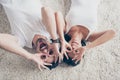 Fun together. Playful couple is lying on the floor on comfortable beige carpet on the floor at home. They are gesturing glasses w Royalty Free Stock Photo