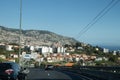 Cityscape over Funchal and its hills from a highway, cars and signs under sun light.