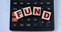 FUND - word on wooden cubes on the background of a calculator