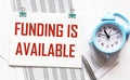 Funding Available, the text is written on a notepad that lies on the financial documents, next to Royalty Free Stock Photo