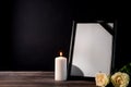 Blank funeral frame, candle and flowers on table against black background Royalty Free Stock Photo