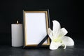 Funeral photo frame with ribbon, white lily and candle on black table against dark background. Space for design Royalty Free Stock Photo