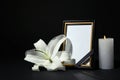 Funeral photo frame with ribbon, white lily and candle on dark table against black background Royalty Free Stock Photo