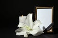 Funeral photo frame with ribbon, white lily and candle on table against black background. Space for design Royalty Free Stock Photo