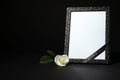 Funeral photo frame with ribbon and white rose on table against black background. Space for design Royalty Free Stock Photo